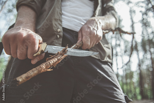 Into the wild. Close up of male hands is sharpening stick with the help of knife. Concept of travel and survival