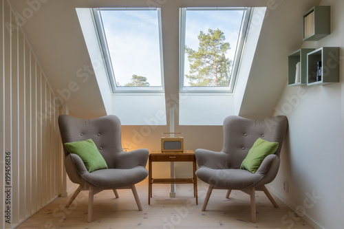 Modern retro design in a attic / loft. Small vintage table with a radio on and two reading chairs under two skylights.