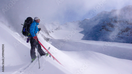 male backcountry skier on a backcountry ski tour playing around during light snowfall on an otherwise beautiful winter day in the Swiss Alps