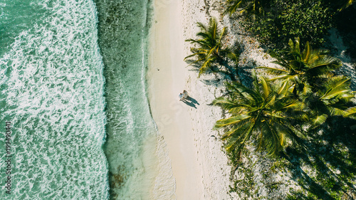 The couple walks on the beach between the ocean and palm trees