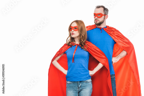 super couple in masks and cloaks standing with hands on waist and looking away isolated on white