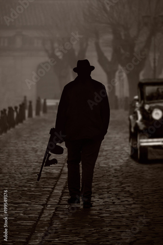 Silhouette of a gangster with machine gun, on a street with fog