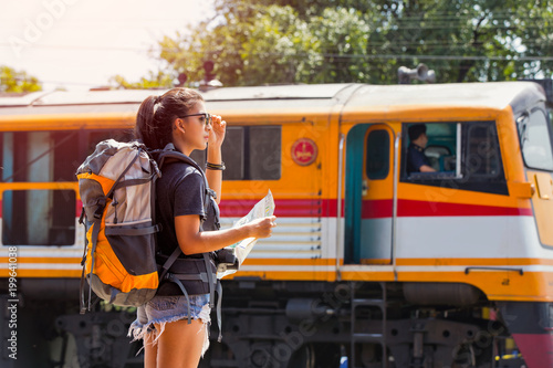 Young asian woman traveler with backpack and sunglass looking the map with train background at Ayutthaya train station.