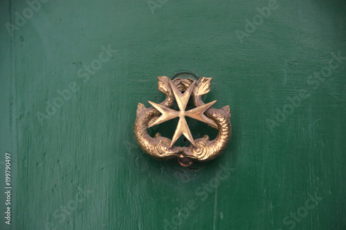 złota kołatka do drzwi w kształcie krzyża maltańskiego na zielonych drzwiach