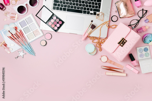 Fashion blogger workspace with laptop and female accessory, cosmetics products on pale pink table. flat lay, top view