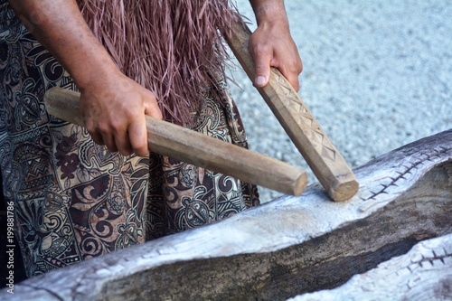 Cook Islander man plays on a large wooden log Pate drum instrument