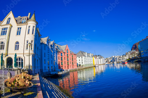 Outdoor blurred view of water canal with houses and port in town on beautiful sunny day in Alesund