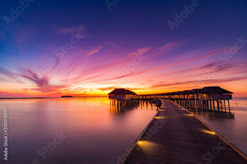 Sunset in Maldives island. Beautiful sunset sky and clouds, luxury water villas and wooden pathway - pier
