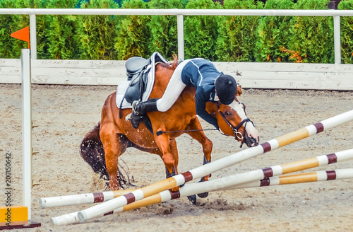 Młody jeździec spada z konia podczas zawodów. Wypadek na skoczni. Tło jeździeckie.