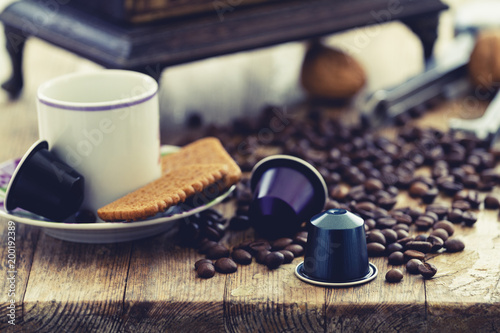 Italian espresso coffee capsules or coffee pods with espresso cups and coffee beans on a rustic wood background. Coffee accessories composition