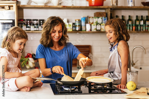 Little sisters cooking with her mother in the kitchen.