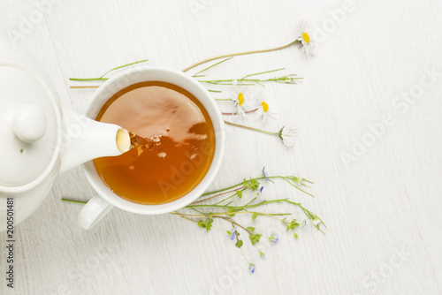 pouring herbal tea into cup on white table