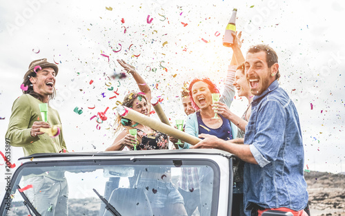 Party people having fun on 4x4 convertible car throwing confetti and drinking champagne