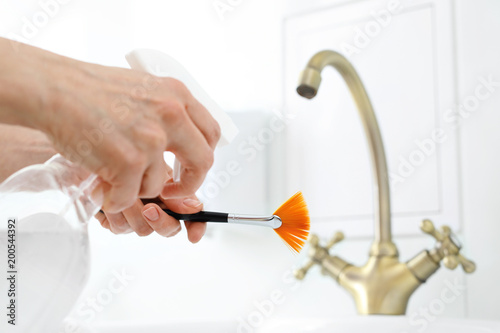 Dezynfekcja narzędzi kosmetycznych. Kosmetyczka spryskuje preparatem antybakteryjnym pędzel.