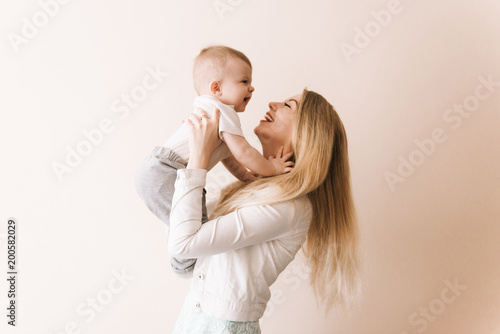 You are my treasure! cheerful beautiful young woman holding baby boy in her hands and looking at him with love at home