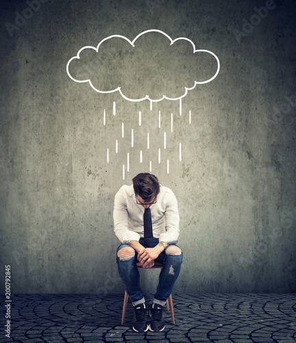 Sad business man sitting on a chair looking down with a rain cloud above him