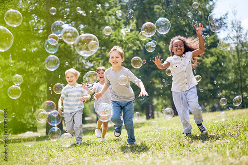 Multi-ethnic group of little friends with toothy smiles on their faces enjoying warm sunny day while participating in soap bubbles show