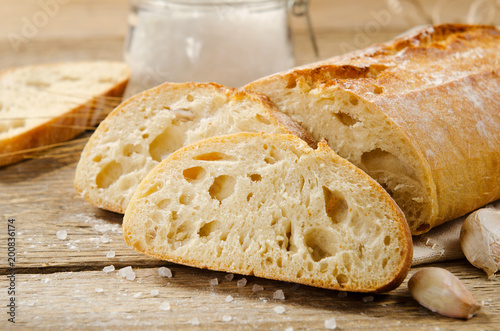 Ciabatta bread. Slices of ciabatta with garlic, salt on wooden table on linen cloth. Rustic style, italian. Close up