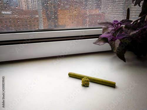 A bud of marijuana and a fresh cigarillo on the window bay. Rainy daytime.