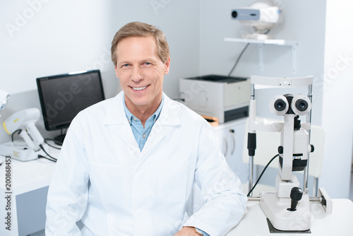 handsome smiling ophthalmologist looking at camera in consulting room