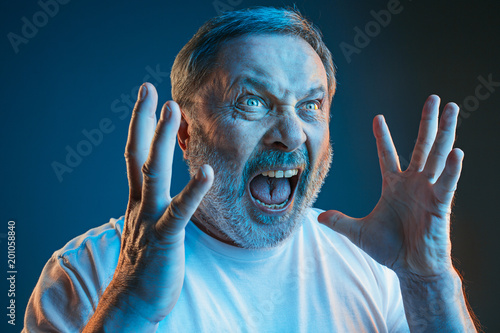 The senior emotional angry man screaming on blue studio background