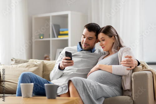 pregnancy, technology and people concept - happy man and his pregnant wife with smartphones at home