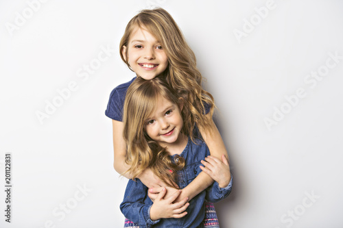 Joyful beautiful child with her sister close to a white wall