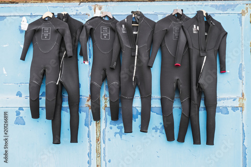 A number of wetsuits drying in summer sun on an old distressed door after use in surfing.