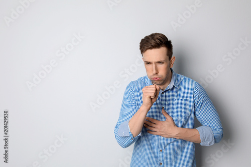 Young man coughing on light background