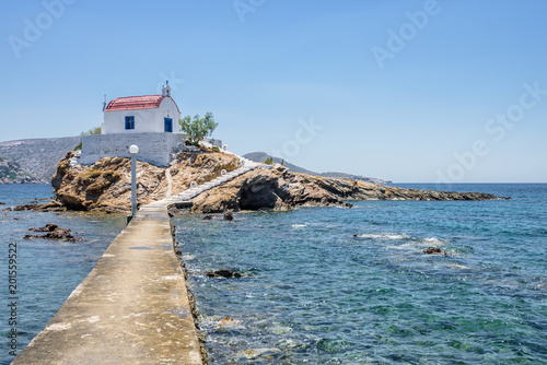 Holy white and blue chruch of agios Isidoros shining at an empty place in the greek sea only reachable by a stone boardwalk over the water on the island of Leros, Dodecanese, Greece