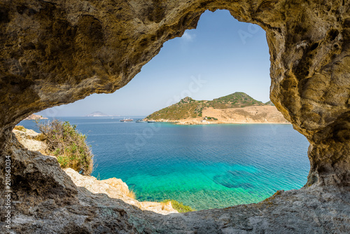 Beautiful sunny view through a rocky cave to the greek blue sea with crystal clear water from an a hill with boats cruising fishing surrounded by mountains, Patmos Island, Kos, Dodecanese/ Greece 