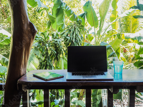 laptop of a digital nomad on a wooden table in nature with a green tropical background