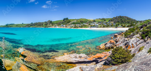 Pretty view to small paradise like town village sandy beach with turquoise blue water and red orange rocks and green shore forest on warm sunny clear sky day, Boat Harbour Beach, Tasmania, Australia