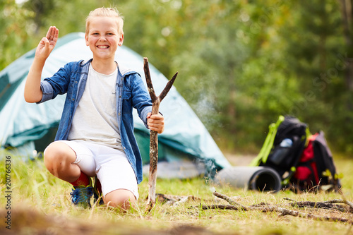 Young boy scout with stick showing open palm and three fingers put together during his backpack trip