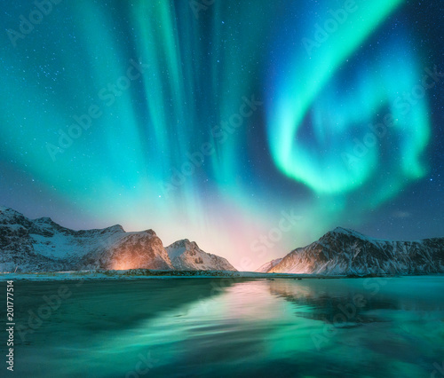Aurora borealis in Lofoten islands, Norway. Aurora. Green northern lights. Starry sky with polar lights. Night winter landscape with aurora, sea with sky reflection, stones, beach and snowy mountains
