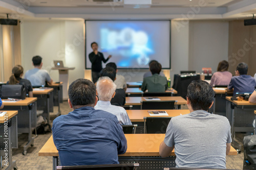 Rear side of Audiences sitting and listening the speackers on the stage in low light meeting room, event and seminar concept