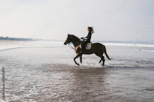 young female equestrian riding horse in water