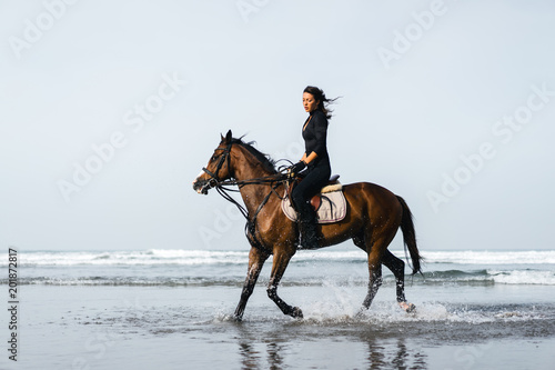 young female equestrian riding horse with ocean behind