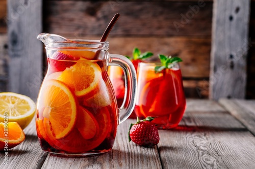 Homemade red wine sangria with orange, apple, strawberry and ice in pitcher and glass on wooden background