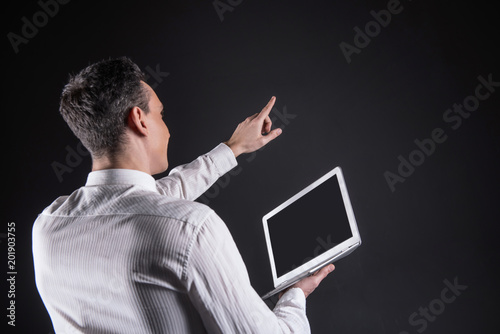 Impressive technology. Joyful positive nice man holding his hand up and pointing at the digital screen while being impressed by modern technology