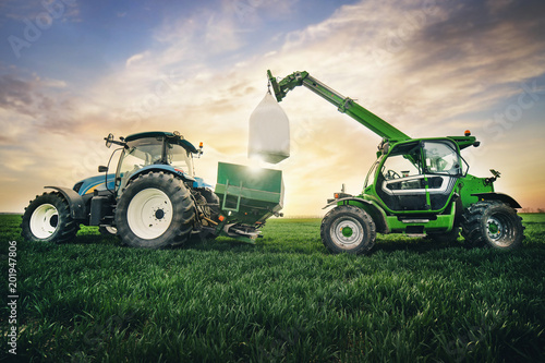 crane puts a sack of fertilizer on a trailer in the field in the spring