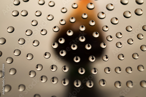 A glass surface with water droplets that reflect the silhouette of the object behind the glass.