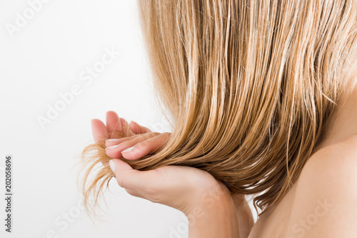 Young woman with hand touching her wet, blonde, perfect hair after shower on the white background. Care about beautiful, healthy and clean hair. Beauty salon concept. Side view.