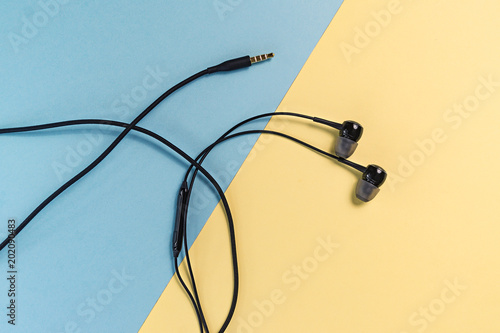 Black earphones on blue and yellow pastel background