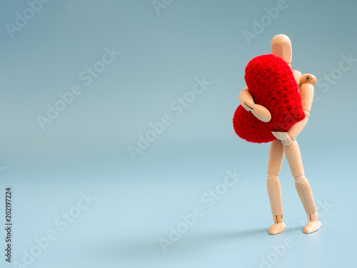 Wooden puppet standing and hold red heart on the sky blue screen background. Wooden puppet handle the heart with love and care. Concept of take care and love.