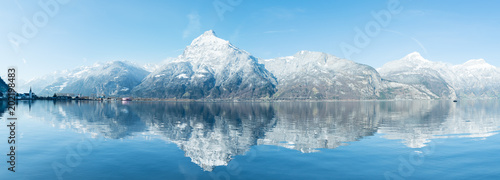 Wide mountain panorama of the Alps in the snow. Grandiose panorama of the snow-capped mountains. Reflections in the water of a mountain lake. Alps in Switzerland. Canton Uri.