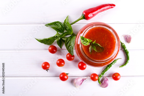 Tomato ketchup sauce with cherry tomatoes and red hot chili peppers, garlic and herbs in a glass jar on white background. Homemade tomato sauce and fresh tomatoes. . Flat lay, top view