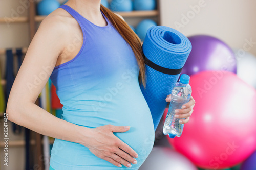 Pregnant sporty woman with a mat for yoga in the hand