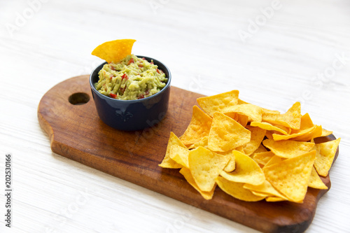 Traditional sauce guacamole with nachos on wooden board on white wooden background. Side view