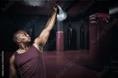 Fit man exercising with dumbbell against red boxing area with punching bags